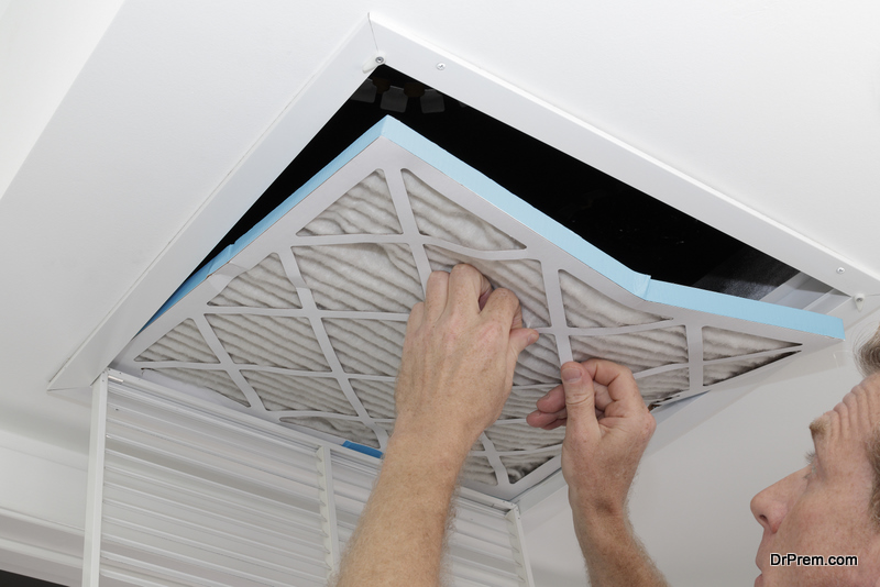 Person removing an old dirty air filter from a ceiling intake vent of a home HVAC system. Unclean gray square furnace air filter being taken out of a ceiling air vent.
