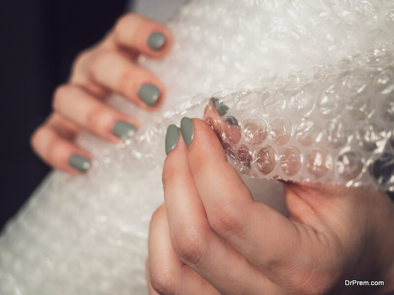 In women's hands, a roll of packaging paper for the delivery of valuable goods, close-up. Girl bursts air bubbles on the package, anti stress.