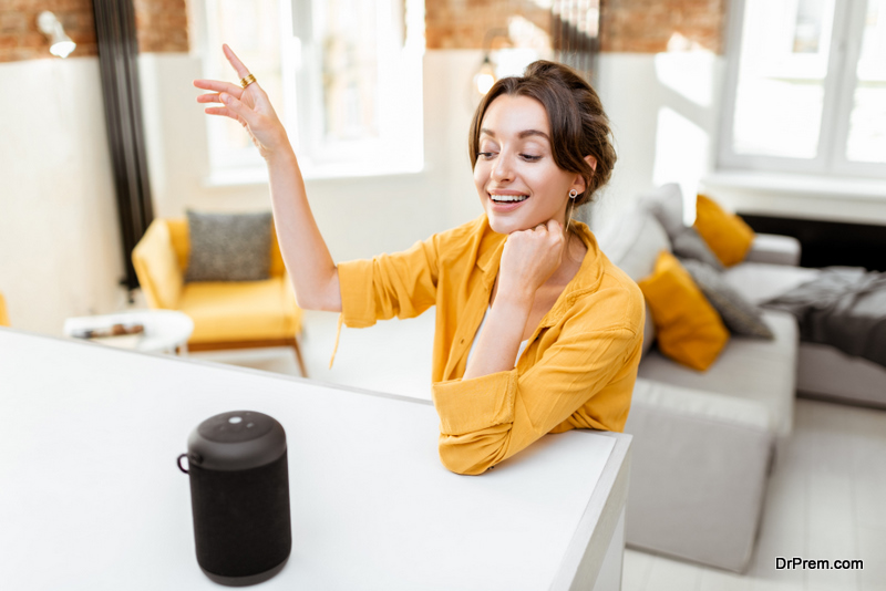 Happy young woman controlling smart home devices with a voice commands and smart speaker at home. Concept of a smart home and managing wireless devices remotely
