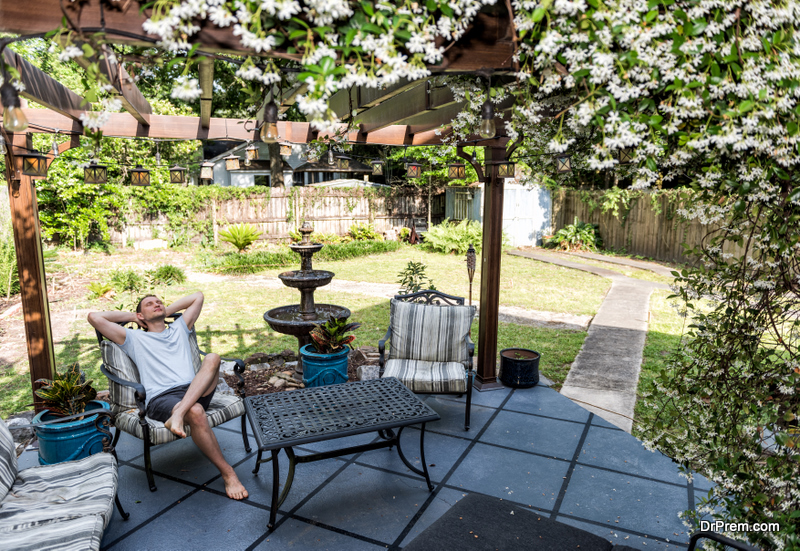 Young man lying down on patio lounge chair in outdoor spring flower garden 