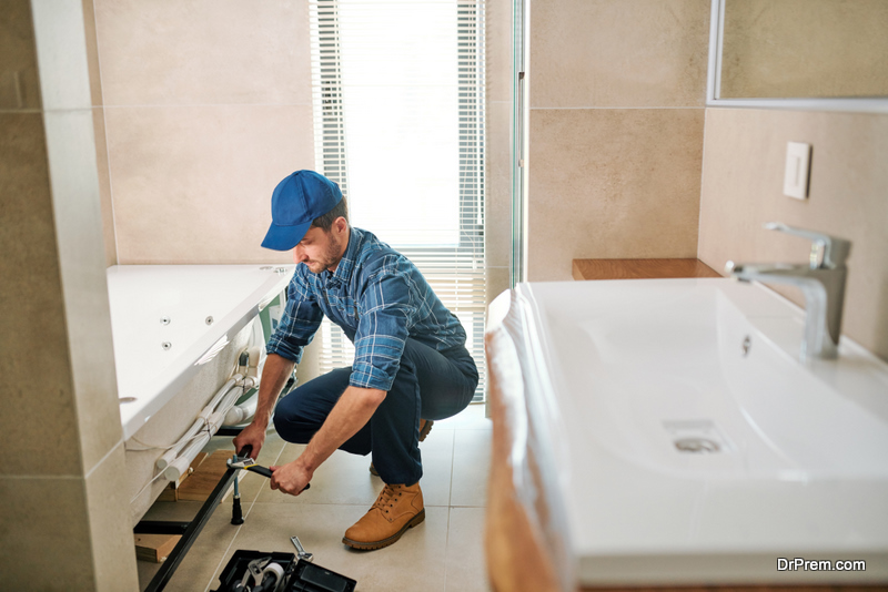 Young worker in uniform sitting on squats while fixing or fastening detail during bathtub installation work