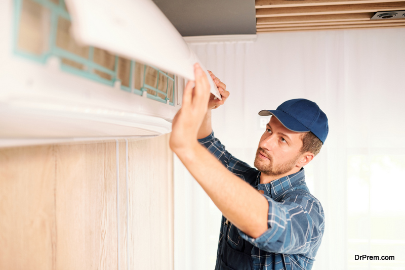 Young electrician or repiar service technician in workwear opening lid of air conditioner to find out problem