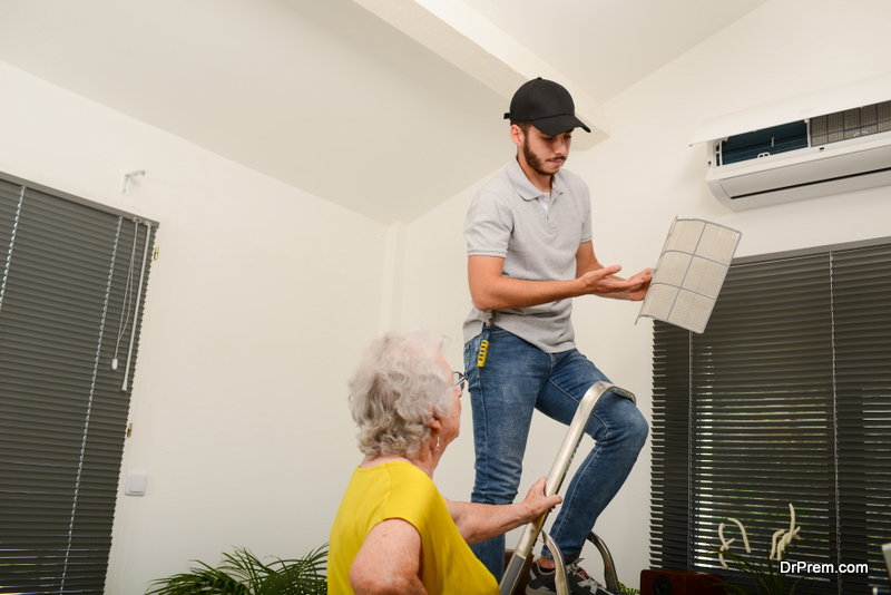 handsome young man electrician cleaning air filter on an indoor unit of air conditioning system in client house with senior woman